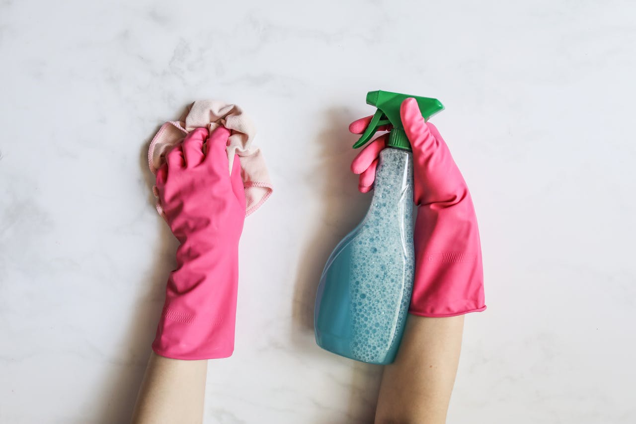 services-04 A pair of hands in pink gloves are cleaning with a spray bottle on a white background.
